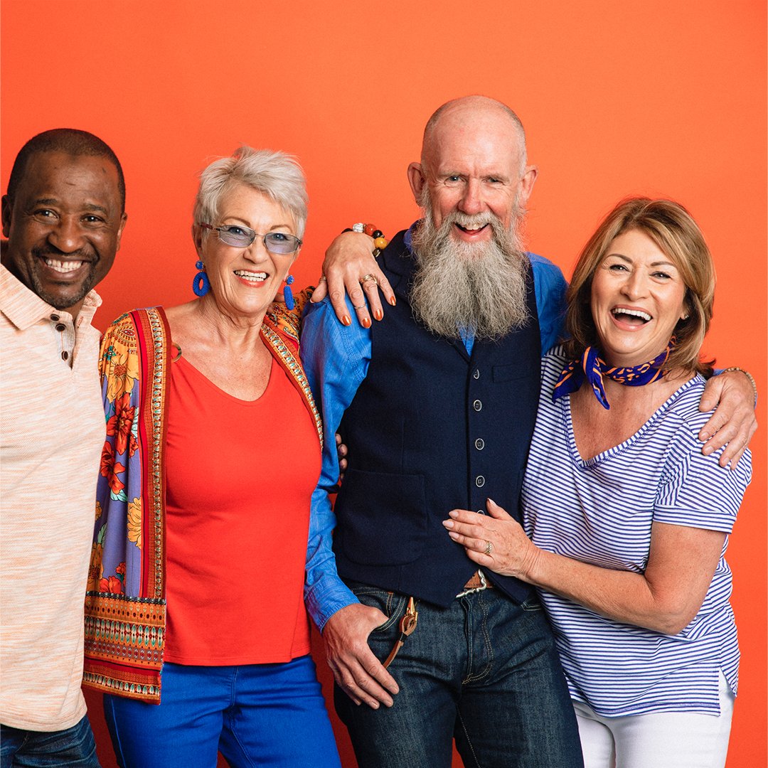 A group of four people standing next to each other and smiling in front of an orange background.