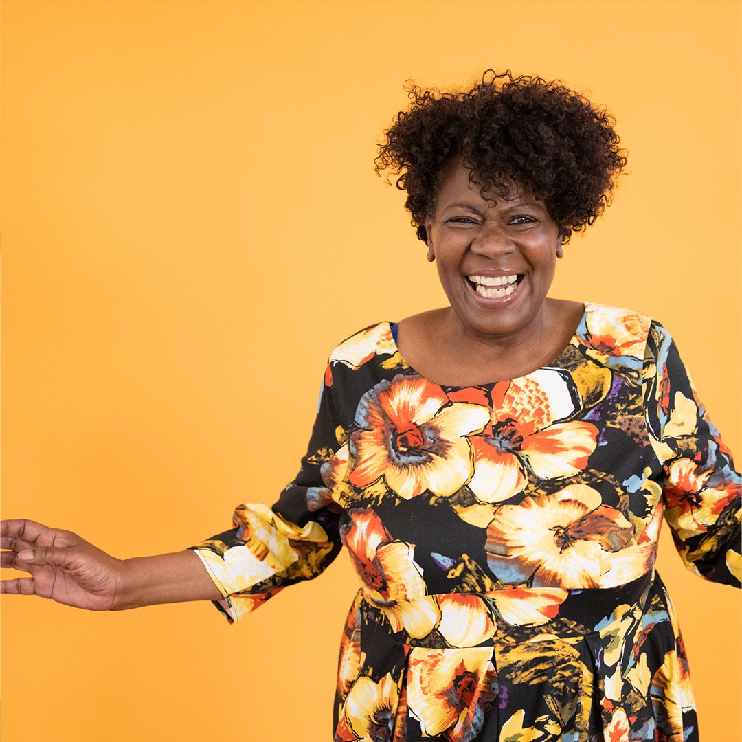 A woman in a floral dress smiling in front of a yellow background.