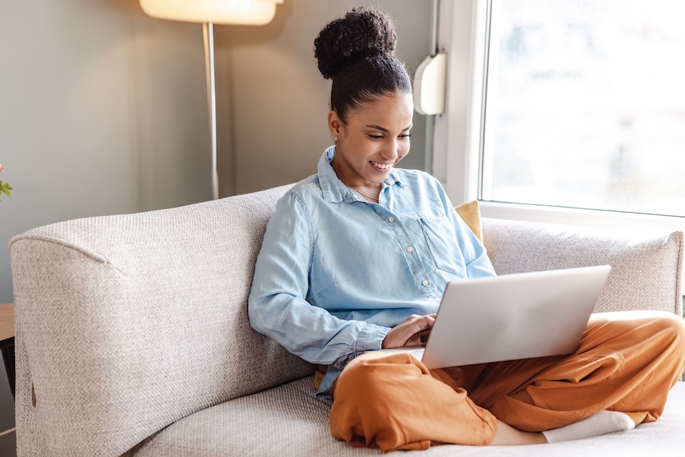 A woman sitting cross-legged on a couch, focused on her laptop..