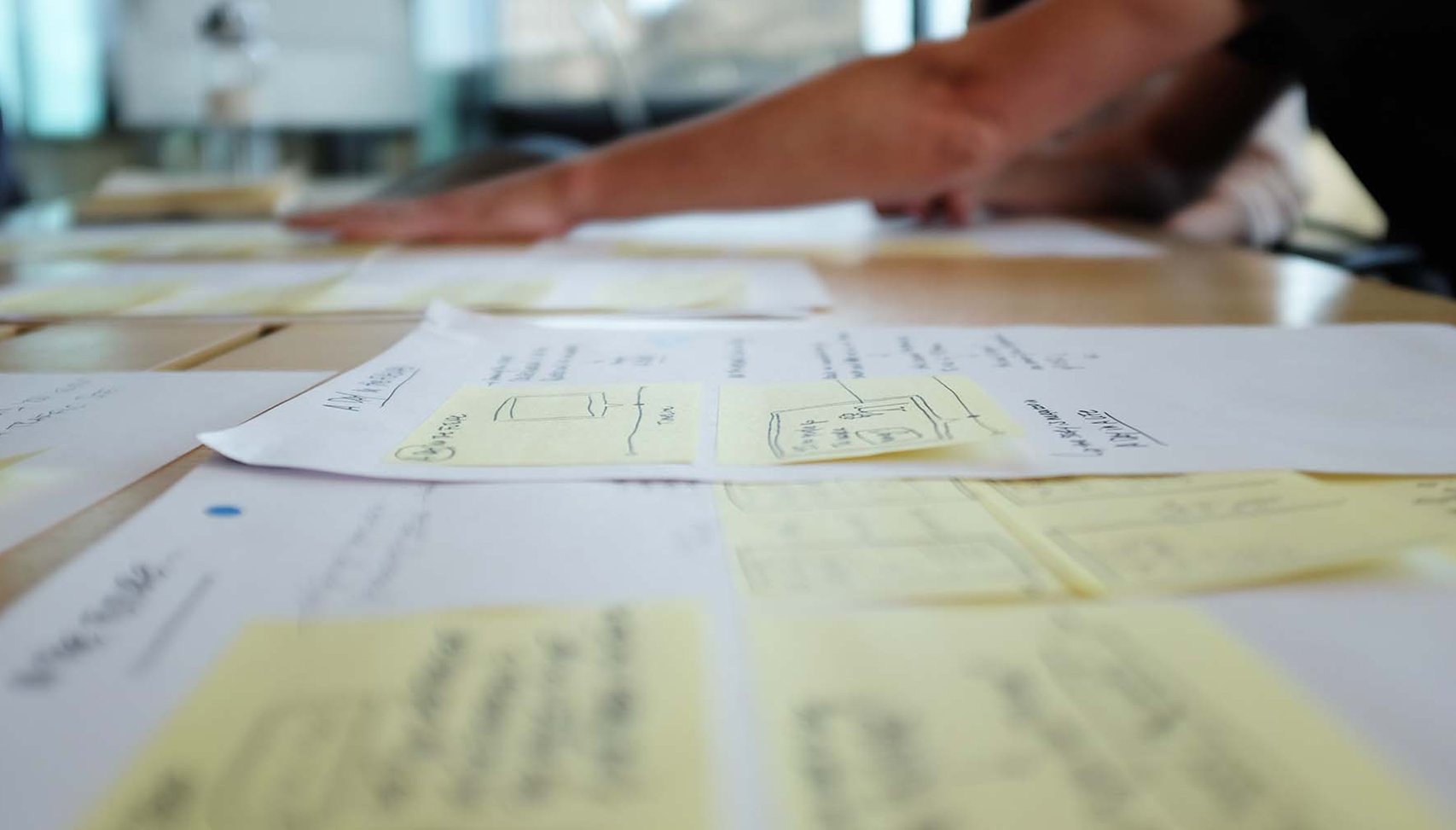 A wooden table topped with white papers and yellow sticky notes.