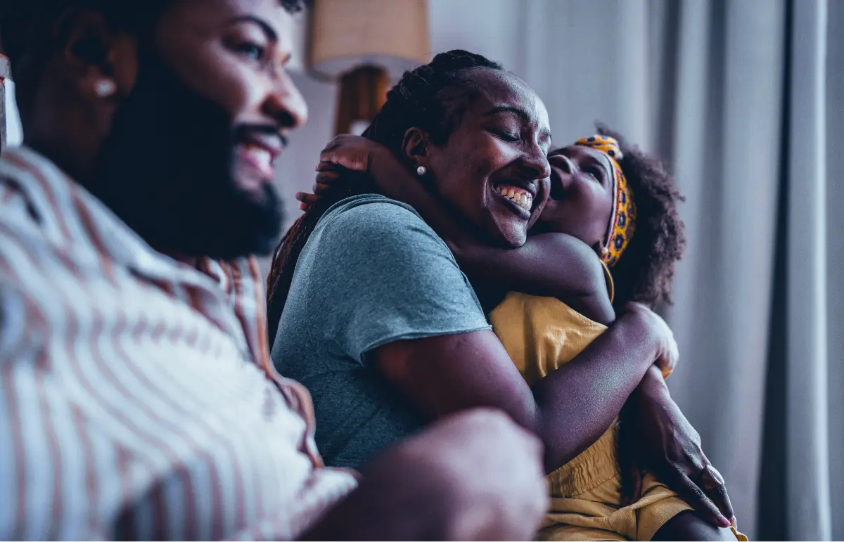 Smiling child hugging an adult woman, with a man sitting next to them