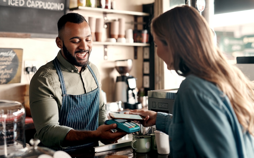 A coffee shop employee taking an electronic payment from a customer over the counter.